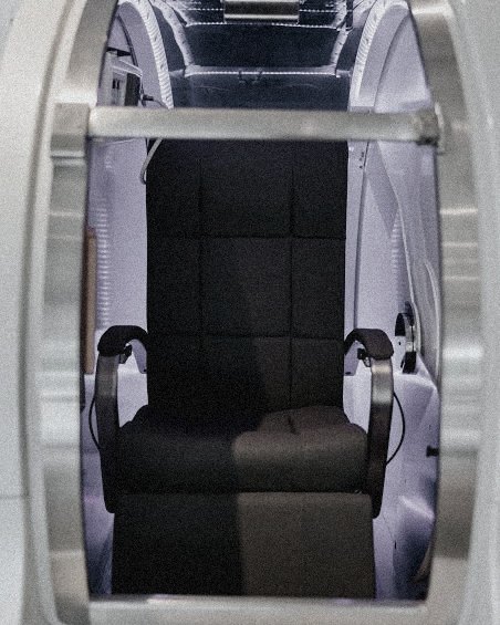 A hyperbaric therapy chamber lit from within, its hatch open to an empty seat.