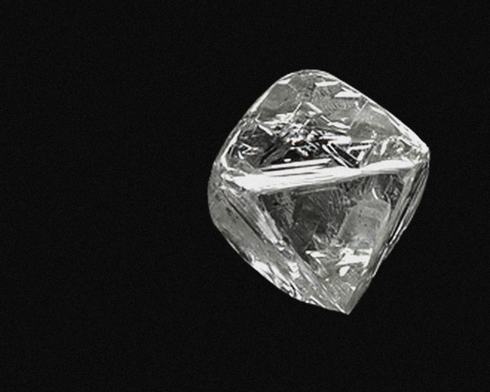 A rough, uncut diamond crystal photographed on a black field, dull and unremarkable.